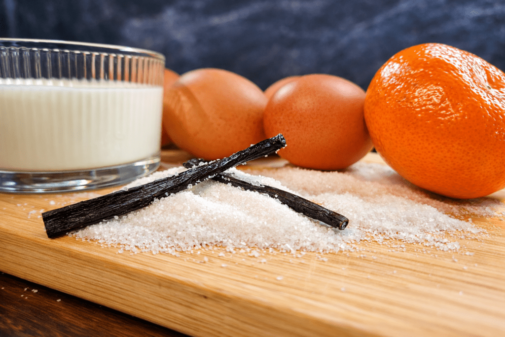 Składniki na creme brulee, jajka, wanilia, śmietana, cukier i mandarynka