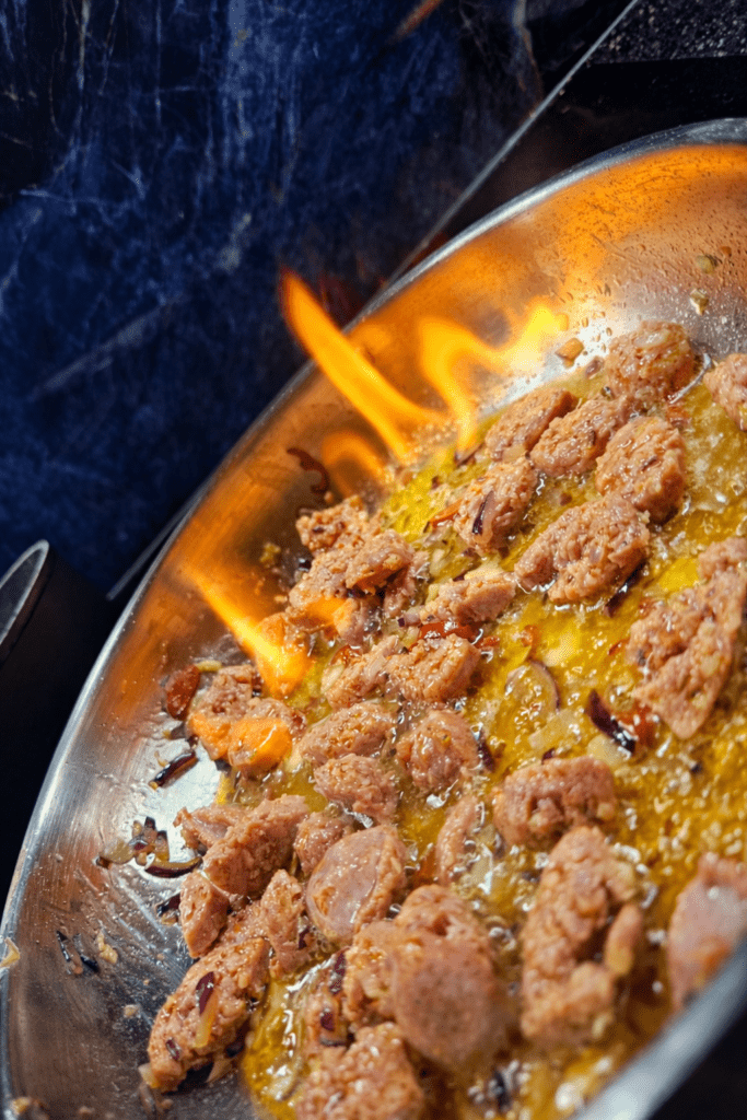 Zdjęcie patalni z smażoną salsicią oraz palącym się alkoholem 
